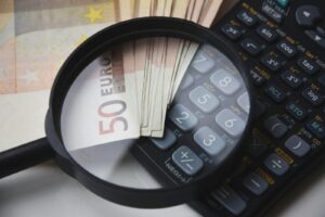 Lupa sobre un billete de 50 euros y una calculadora financiera negra, imagen relacionada con los mejores programas de contabilidad para pymes y el control de gastos y finanzas.