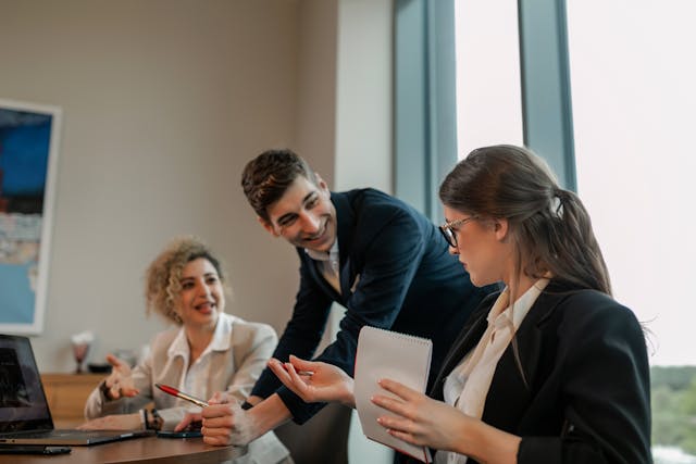 Equipo de trabajo en una reunión de oficina con tres personas, un hombre señalando una libreta mientras dos mujeres utilizan una laptop, colaborando en la automatización de procesos empresariales