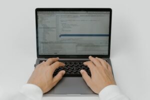 Vista cenital de unas manos de un desarrollador sobre el teclado de un portátil abierto. La pantalla muestra un entorno de desarrollo integrado con código fuente estructurado y una jerarquía de archivos a la izquierda. Esta imagen representa la fase de desarrollo y personalización al configurar integraciones complejas usando n8n para empresas.