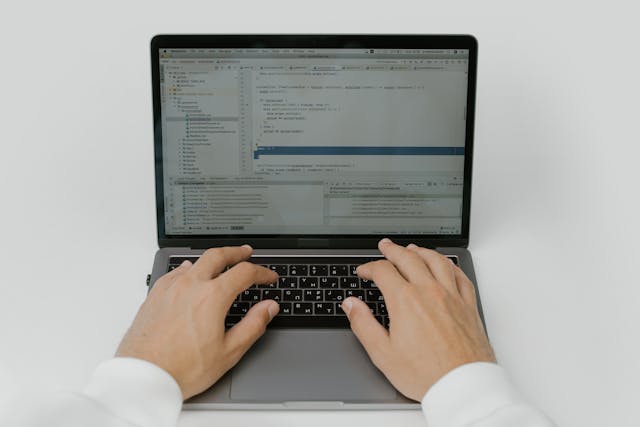 Vista cenital de unas manos de un desarrollador sobre el teclado de un portátil abierto. La pantalla muestra un entorno de desarrollo integrado con código fuente estructurado y una jerarquía de archivos a la izquierda. Esta imagen representa la fase de desarrollo y personalización al configurar integraciones complejas usando n8n para empresas.
